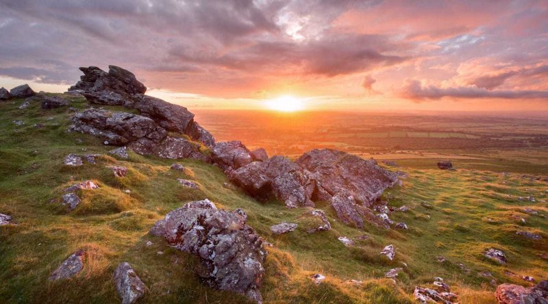 Vivid sunset fron Sourton tor, a large pile of grey granite boulders on the top of a small hill, with the sun just over the horizon and a pink and purple sky overhead, taken in Dartmoor national park in Devon uk