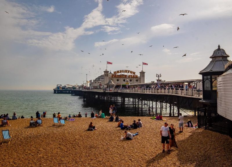 Brighton pier, a wooden pier with white trim on a shingle beach with seagulls flying over it.