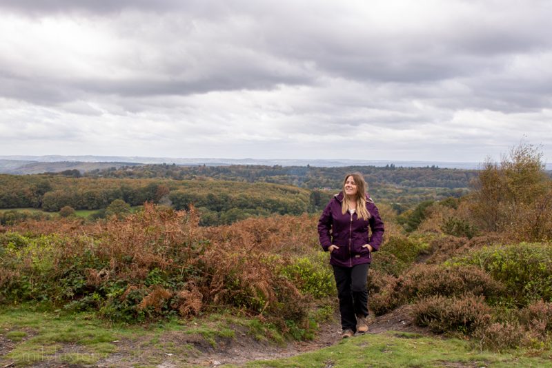 Girl wearing purple parka jacket and black walking trousers with long blonde hair hiking in the South Downs 