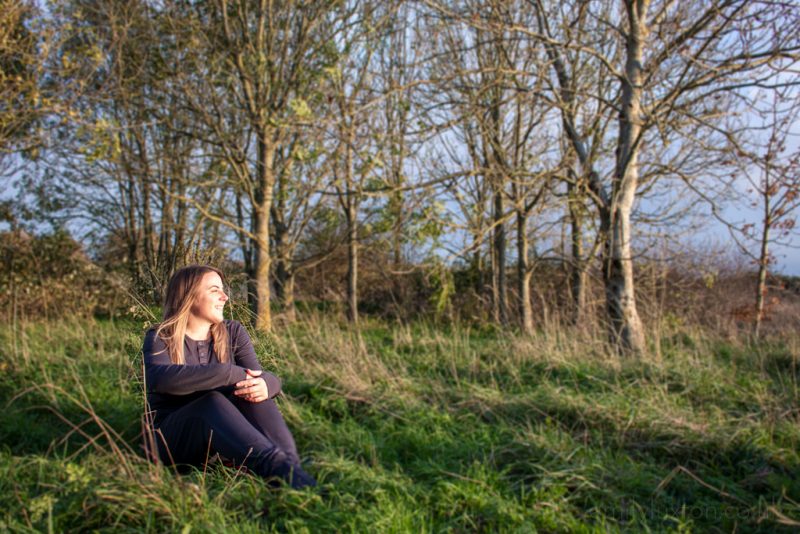 emily wearing grey cotton pyjamas matching top and bottom sitting in a field in front of some trees