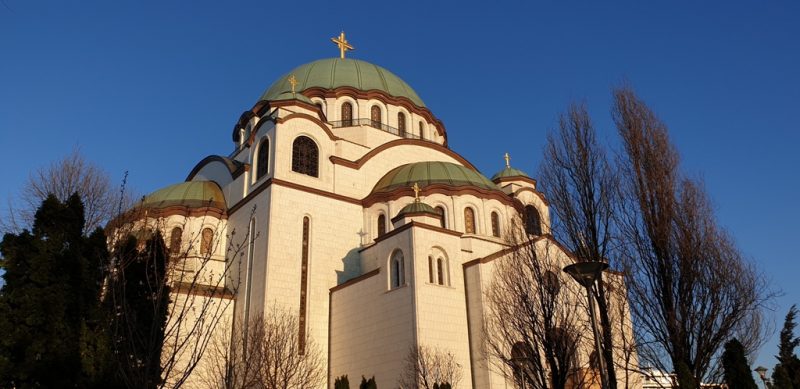 The Church of Saint Sava in Belgrade, Serbia, with white stone walls and green domes, under a clear blue sky