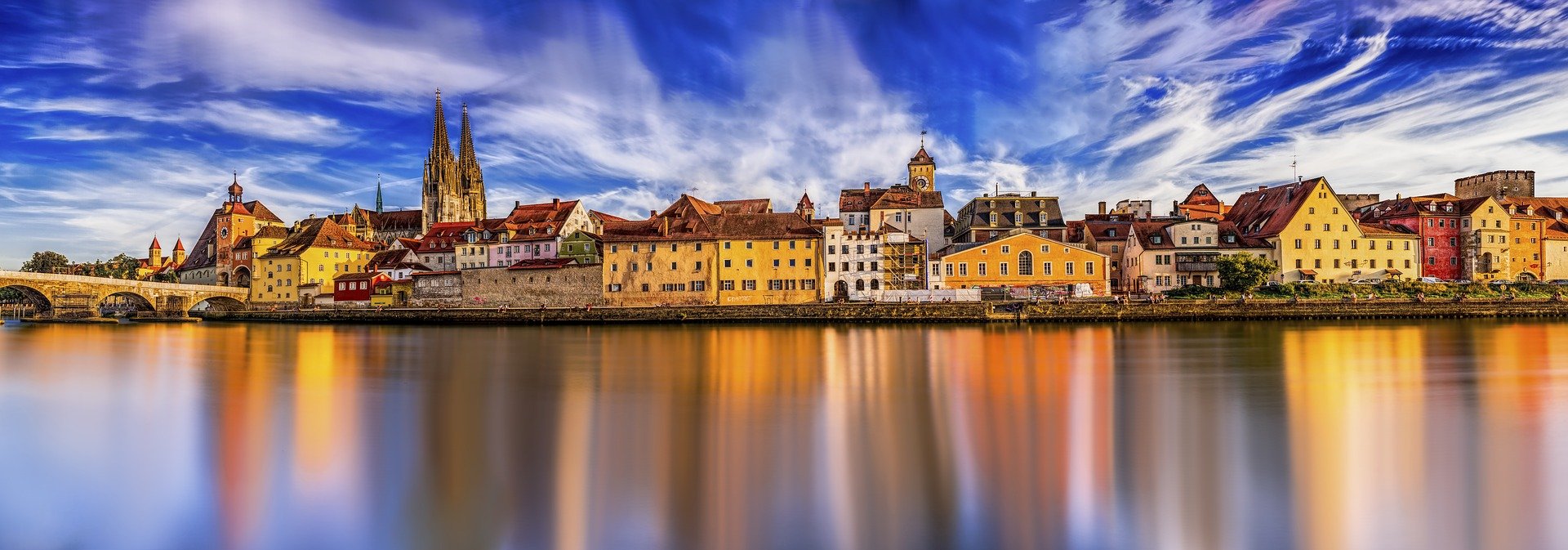 Panorama of a river with a city on the far site with many yellow nad orange buildings and a stone church spire to the left. Best River Cruises in Europe