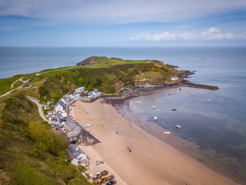 aerial shot of the Llyn Peninsula with a long strip of golden sandy beach running along the edge of a grassy peninsula in wales on a cold day with a slightly cloudy blue sky