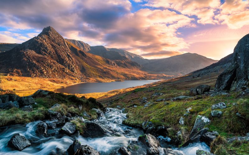 a stream running down to a lake in front of a mountain at sunset in snowdonia - uk adventure bucket list