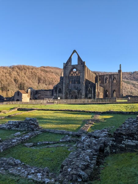 Ruined abbey in a grass field with a hill behind
