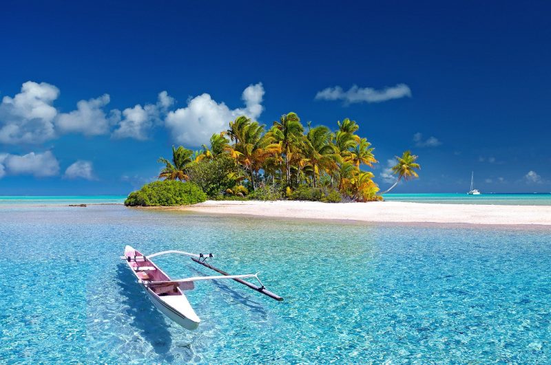 boat in clear turquoise sea in front of small island full of palm trees