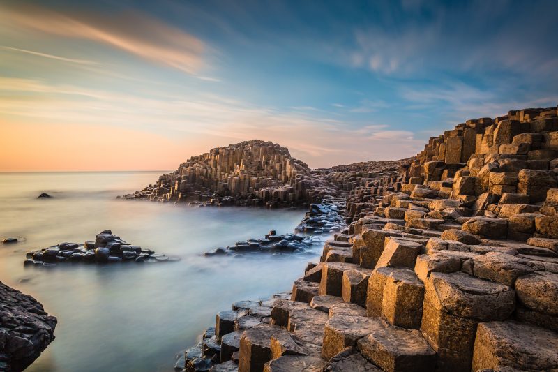 hexagonal shaped stacks of rock in front of the sea which is misty because of a long exposure at sunset in northern ireland uk