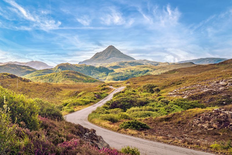 a road leading through moors towards a distant peak beneath a blue sky - an adventure road trip in Scotland UK