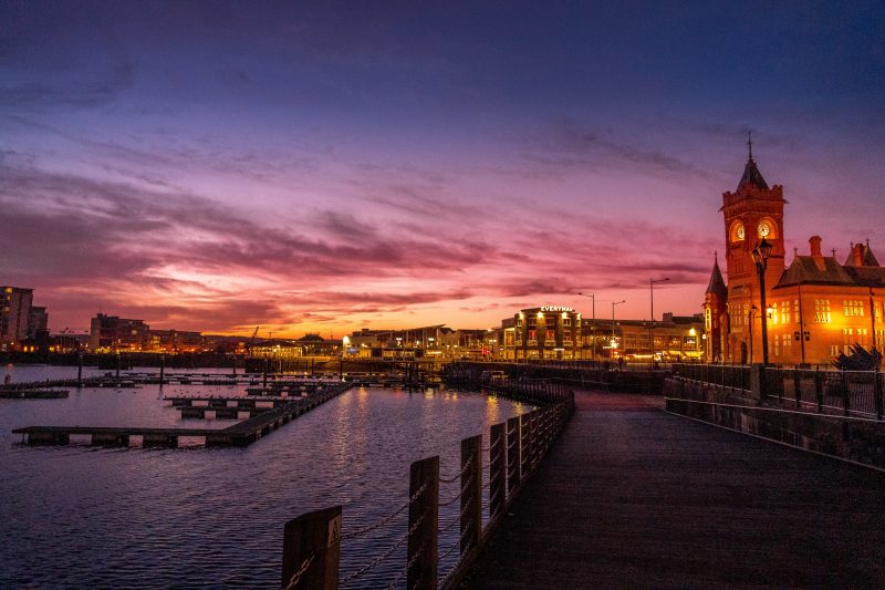 Cardiff Bay at Night with a square clock tower built from red stone lit up against a purple sunset sky