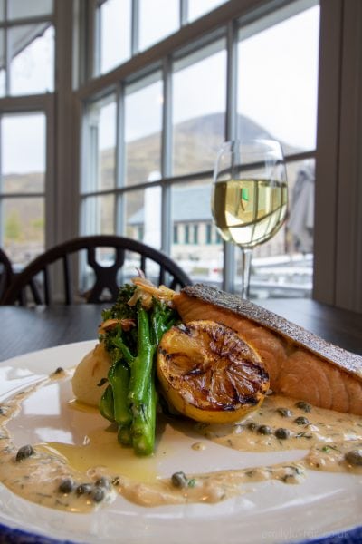 Salmon and broccoli with a glass of wine beside a window at Cluanie Inn