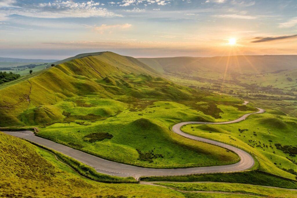 winding country road next to a grassy hill in the peak district at sunset
