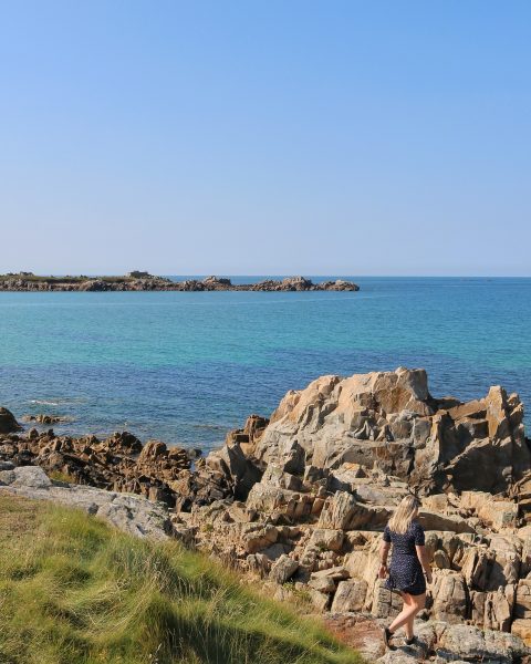 girl walking towards some rocks with the sea in the background