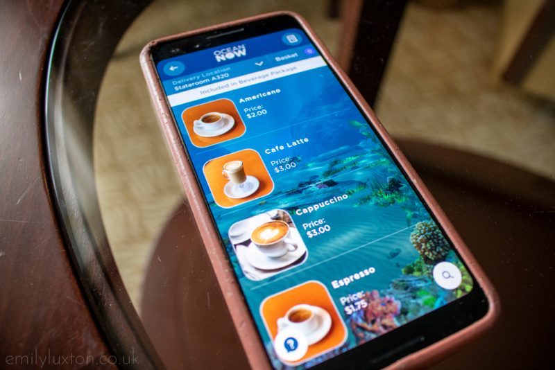 Close up of a phone on a table top with a menu app open showing different coffees available to order. MedallionClass App Princess Cruises