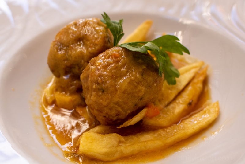 2 light brown balls of cuttlefish meat on top of some chips in a brown sauce in a white bowl