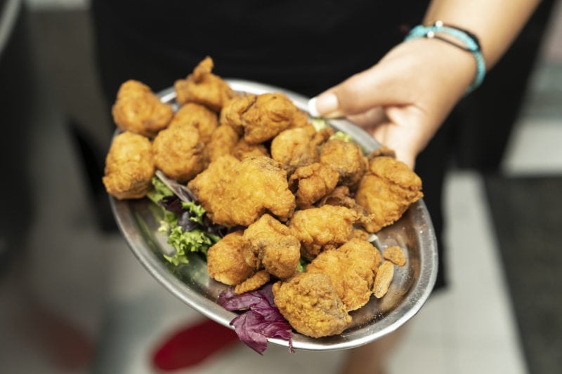 hand holding a silver plate with small chunks of fried battered dogfish called cazon en adobo a popular Andalucian food