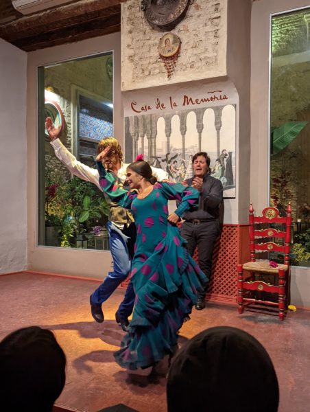 A flamenco dancer in Seville in a long turquoise dress leaning back with one arm raised. there is a male dancer behind her in a waistcoat. 