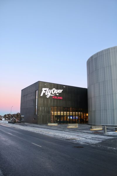 Black building with a sign saying Flyover Iceland with a pink winter sky in Reykjavik