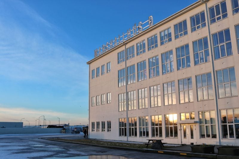 A large white building in front of a blue sky with lots of windows reflecting a winter sunset in Reykjavik harbour district