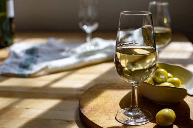 close up of a small glass filled with white sherry next to some olives