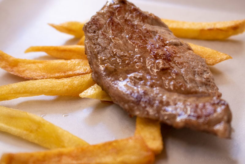 Close-up of grilled brisa iberica ham with french fries on a white plate