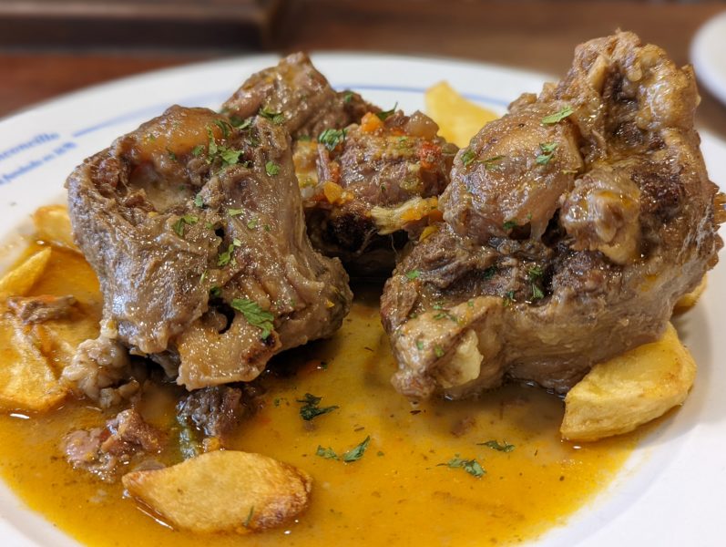 Large cuts of meat on the bone with French fries on a plate filled with sauce, oxtail is a popular food in Seville, Spain