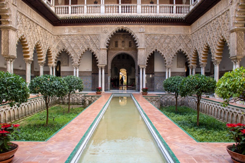 A long rectangular pool of water in the centre of a courtyard with stone arches around it in the centre of a palace