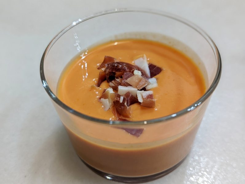 Close up of tomato soup in glass bowl topped with ham pieces, a traditional Seville food called salmorejo 