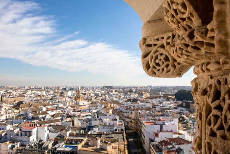 Seville city view seen from a cathedral tower with a  part of the carved beige stone tower visible on the right of the frame. 