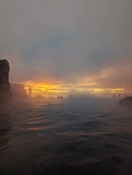 winter sunset seen through the mist and silhouettes of people in the water at Sky Lagoon Reykjavik