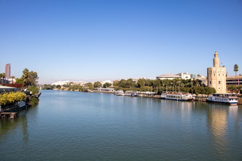 A still blue river on a clear winter day in Seville with a tower on the bank on the right