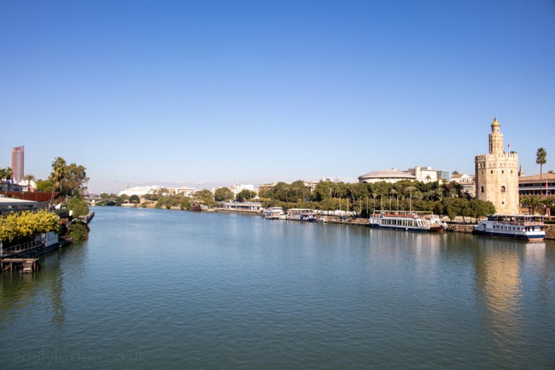 A still blue river on a clear winter day in Seville with a tower on the bank on the right