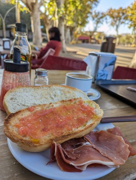 toasted bread topped with pulped tomato next to some serrano ham on a table in a plaza in Seville