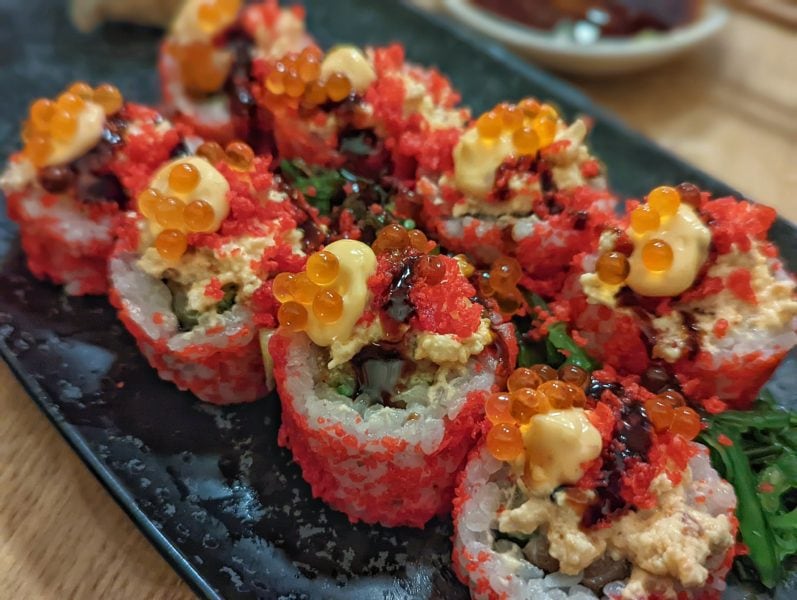 close up of pink maki on a black plate topped with orange salmon roe