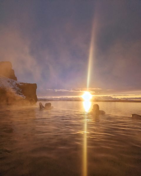 sun setting over the sea behind an infinity pool edge with silhouettes of people seen through steam at Sky lagoon Reykjavik Iceland