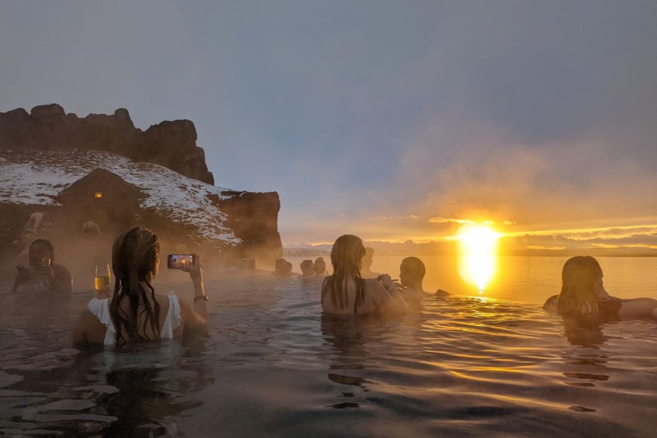 silhouetted people in an infinity pool in front of the sun setting into the sea at Sky Lagoon in Reykjavik Iceland