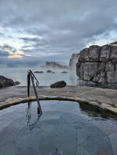 circular pool with cliffs and a larger infinity pool behind it under a grey cloudy sky