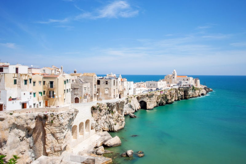white cololured buildings on a rocky peninsua overlooking turquoise sea in puglia italy 