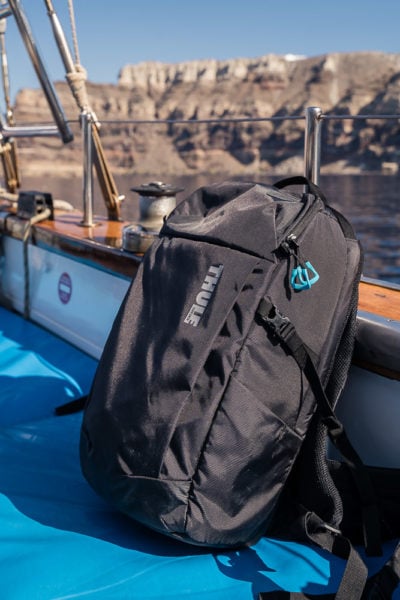 close up of a black Thule camera backpack on the edge of a boat with the sea and rocks in the background