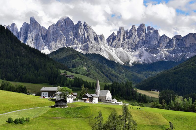 grey rocky mountain peaks behind green hills with a small village and church steeple in front