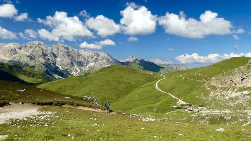 person walking on a trail in the Dolomites with blue sky and mountains behind - best walking holidays in Italy