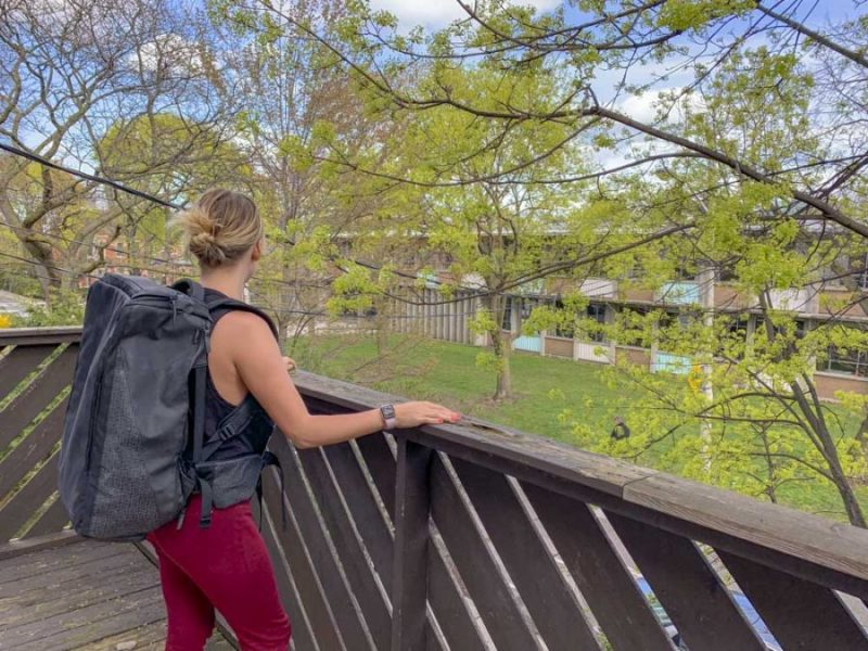 girl wearing red jeans and a black vest top standing on the edge of a wooden balcony wearing a large black cabin backpack