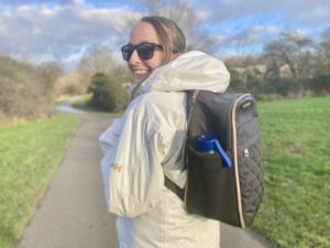 Girl walking in a park in a white rain coat with a black backpack on