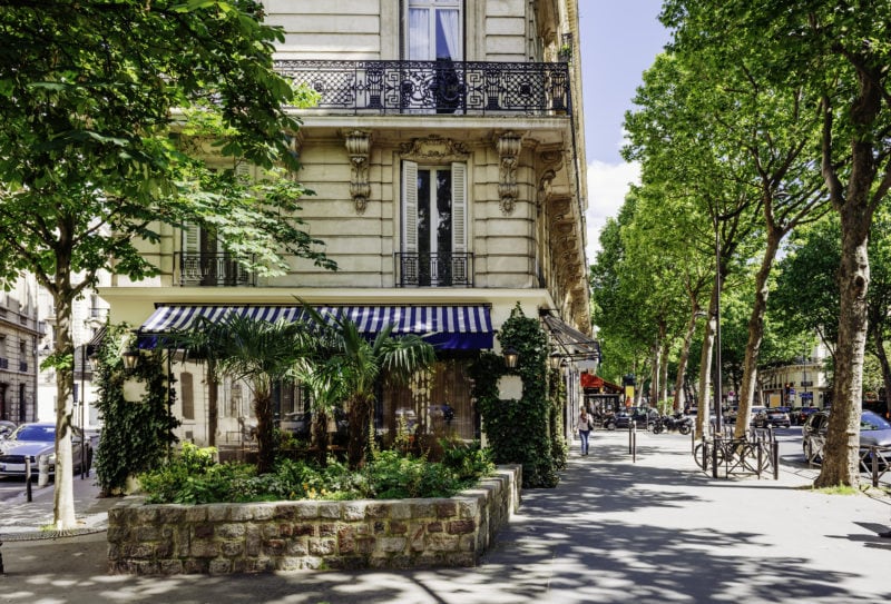 a shop with blue and white awning on a tree lined street in paris france
