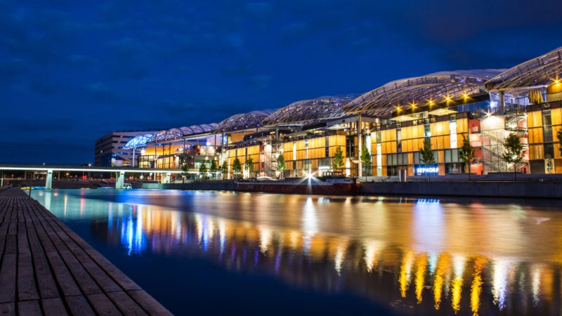 a shopping centre in lyon france lit up at night and reflected in a calm river