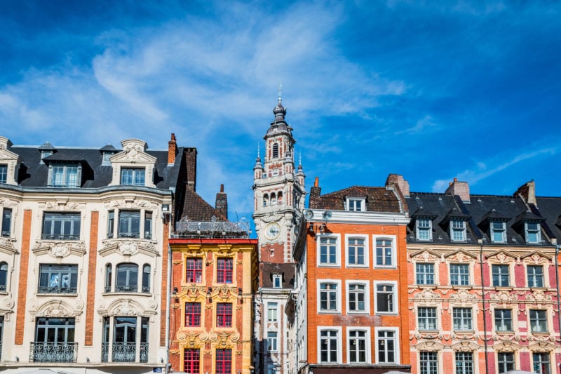 colourful buldings in a row with a red and grey clock tower behind against a blue sky