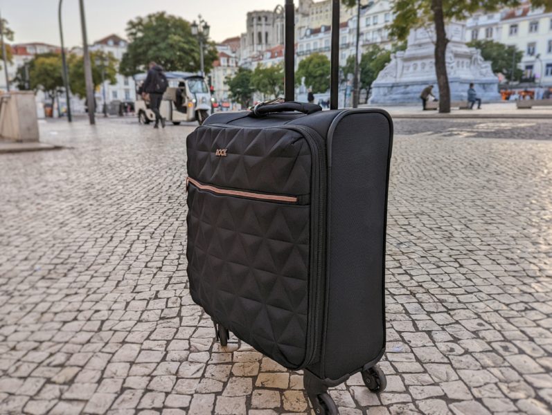 a black suitcase with rose gold zip on a cobbled street with trees behind, one of the best carry on bags for women