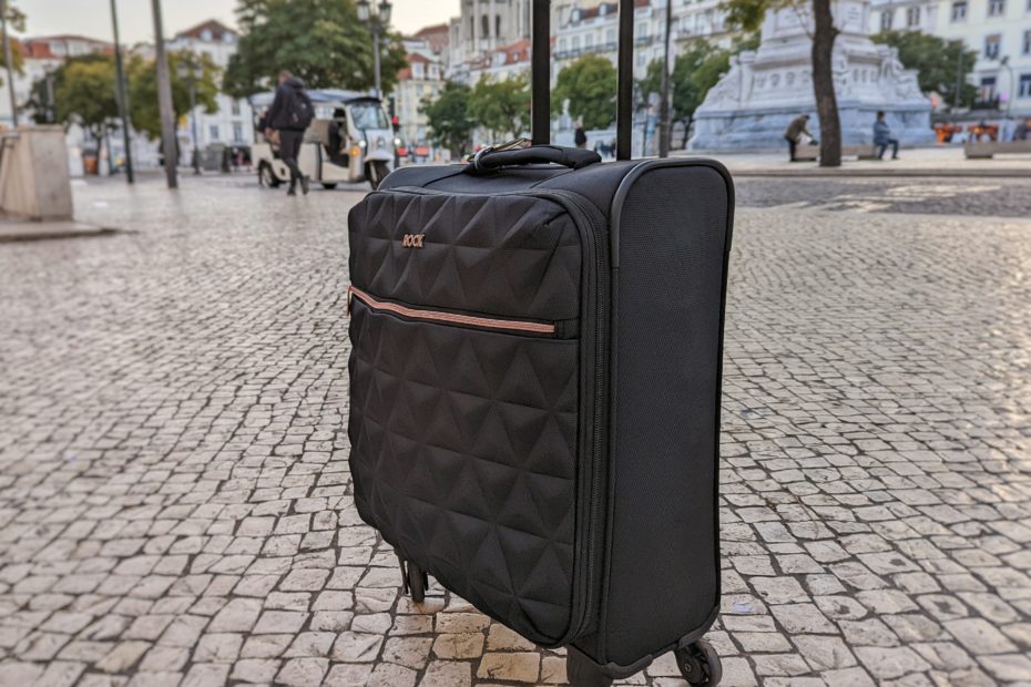 a black suircase with rose cold zip on a cobbled street with trees behind, one of the best cabn bags for women