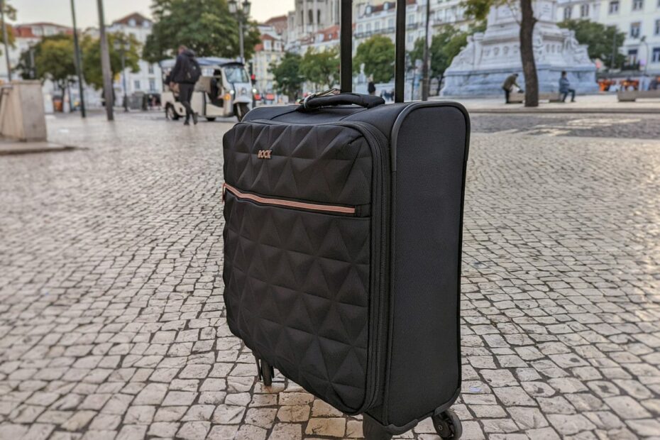 a black suircase with rose cold zip on a cobbled street with trees behind, one of the best cabn bags for women
