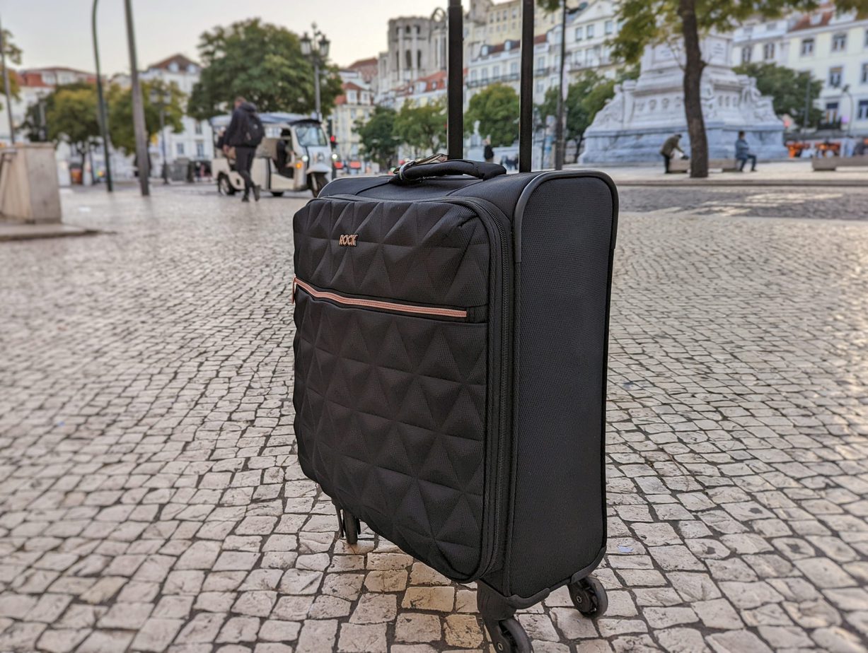 a black suircase with rose cold zip on a cobbled street with trees behind, one of the best cabn bags for women