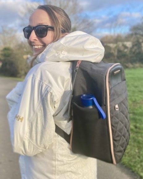 Woman wearing a white jacket and a black backpack turning to smile at the camera